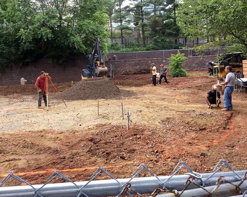 Adamo Brothers crew grading a cleared lot with a surveyor's level, excavator and string lines set out