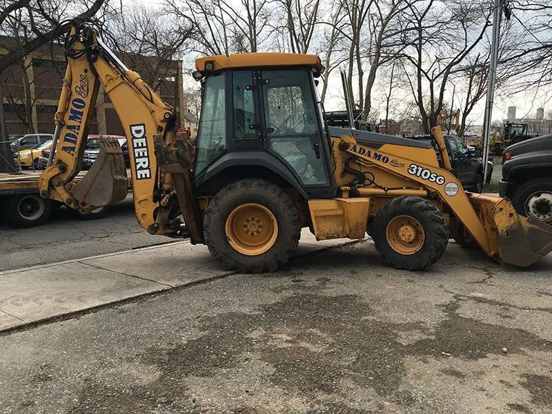 Adamo Bros branded John Deere 310SG backhoe loader parked roadside in Ridgefield, New Jersey